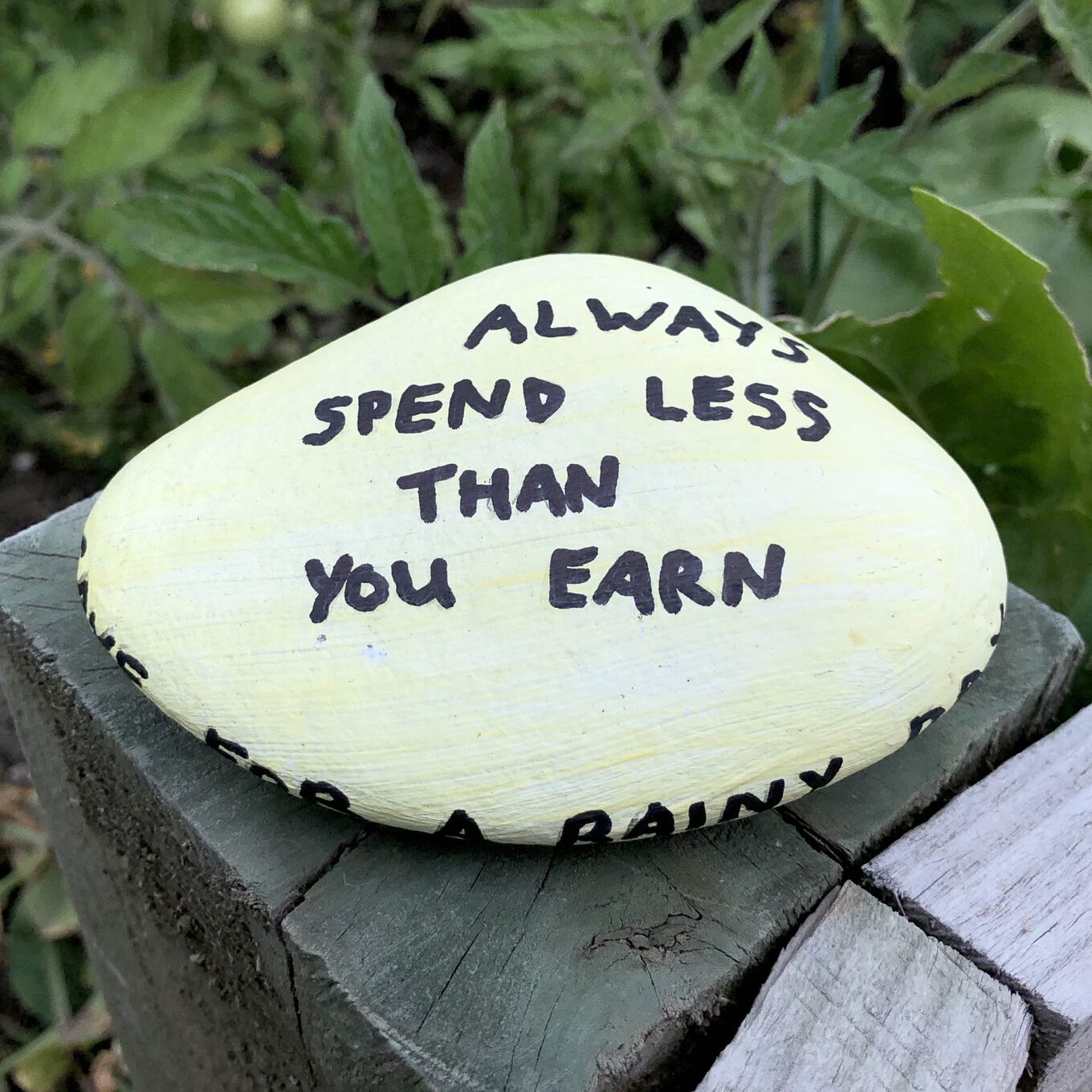 A painted rock that says "Always spend less than you earn"