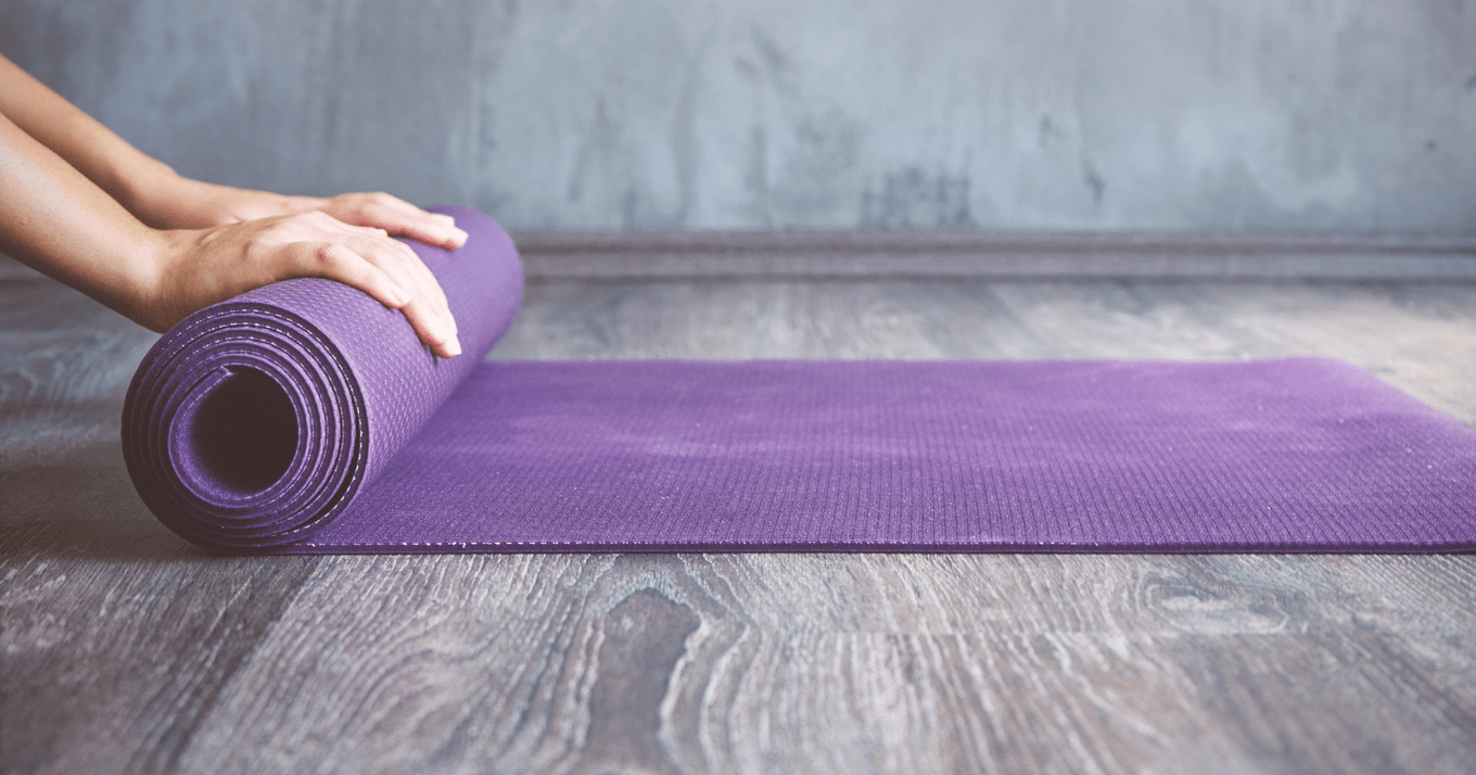 A purple yoga mat is being rolled up